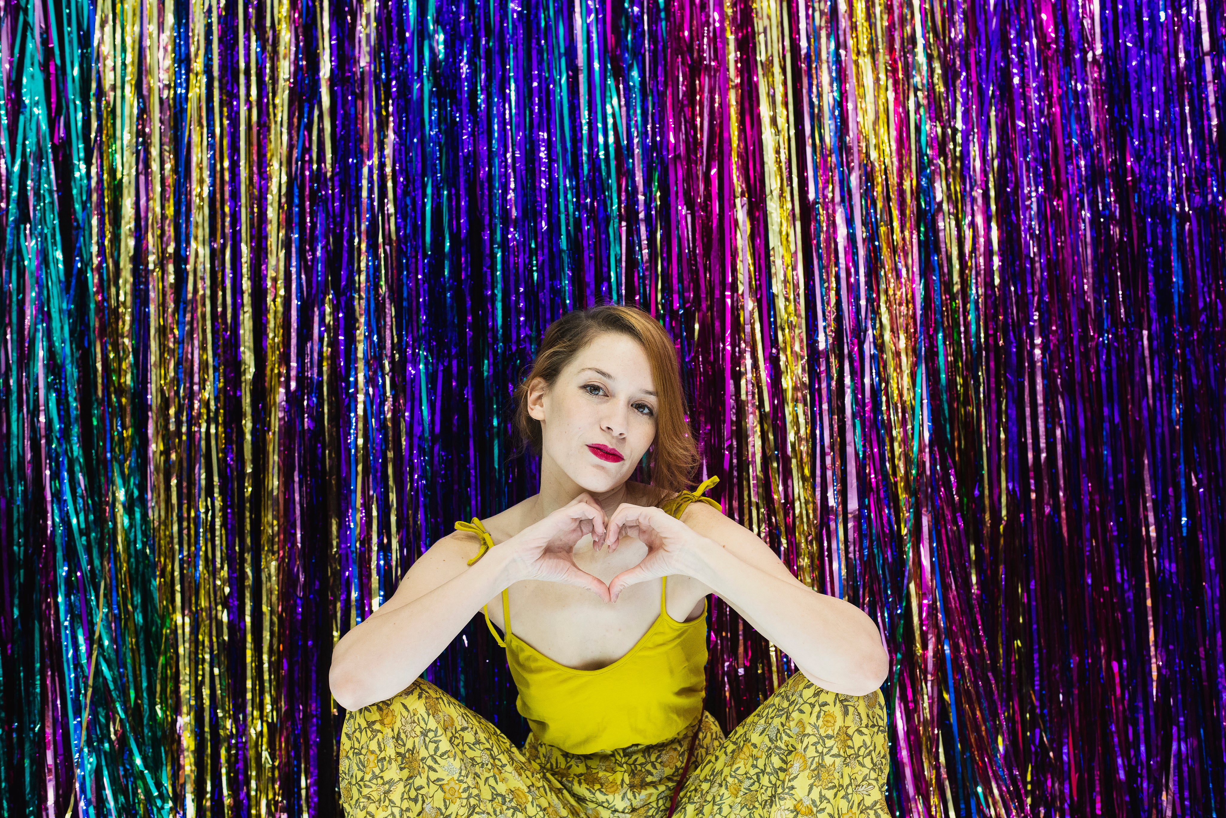 files/woman-makes-hand-heart-gesture-in-front-of-rainbow-wall.jpg